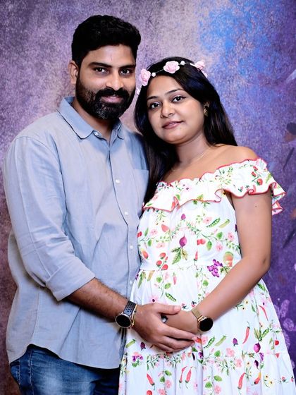 A happy couple portrait from a maternity session. The floral dress and matching flower crown add a fresh, joyful feel against the soft purple backdrop.