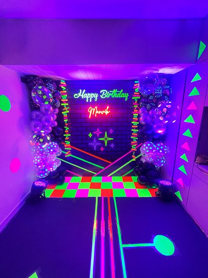 A full view of the immersive neon party room. The glowing checkered dance floor, geometric wall patterns, and vibrant balloon arrangements created a perfect setting for a glow-in-the-dark celebration.