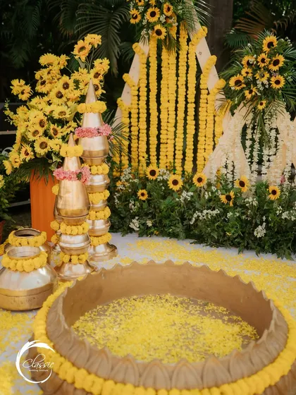 A close-up of the traditional elements. I stacked and decorated brass matkas with marigold garlands and pink flowers, placed next to a large vessel filled with turmeric-colored water and petals for the ceremony.