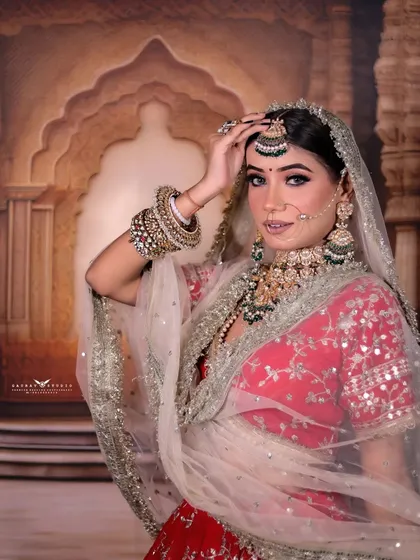 An elegant portrait of the bride adjusting her maang tikka, with the sheer dupatta creating a soft frame.