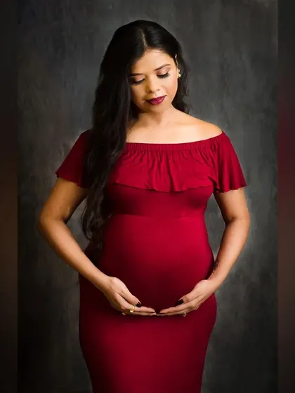 A classic standing pose that beautifully showcases the baby bump. The off-shoulder red gown and the simple, dark background create an elegant and timeless maternity photograph.