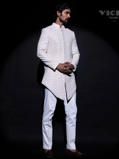 Modern architecture in tailoring. This white sherwani features a striking asymmetric hemline and all-over geometric embroidery, crafted for the groom who appreciates contemporary design.