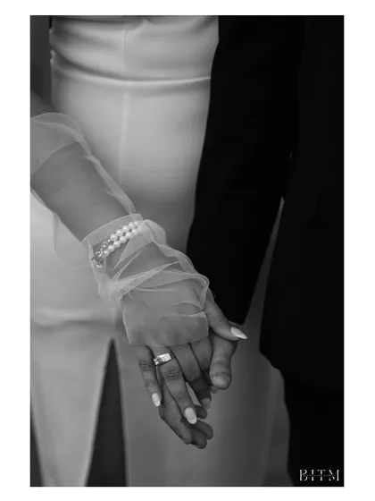 A close-up in black and white, focusing on the couple's intertwined hands. This shot highlights the details: the engagement ring, the delicate gloves, and the simple act of holding on to each other.