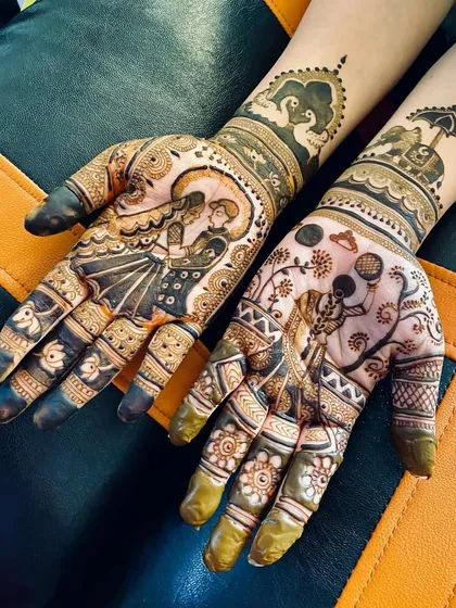This Karvachauth design features a romantic couple portrait on one hand and a woman with a chalni on the other. The arms are adorned with elephant and peacock motifs, adding to the festive grandeur.
