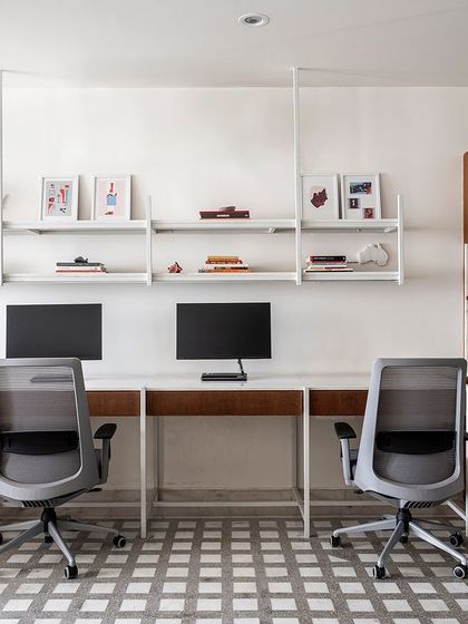 The main workstation area in the 'On The Grid' office is designed for efficiency and collaboration. We used white metal desks with marble tops and ceiling-suspended open shelves to maintain a clean, airy aesthetic, ensuring the 700 sq. ft. space feels uncluttered and productive.