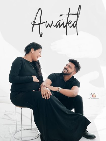Titled 'Awaited', this image captures the happy anticipation of the couple. They share a laugh in a relaxed, seated pose, their joy evident.