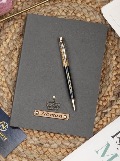 A grey personalized leather diary and pen set with a crown charm.