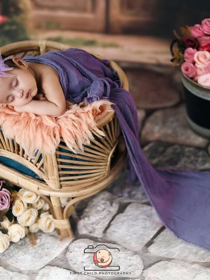 A wider view of the dreamy floral setup. The long, flowing purple fabric adds a touch of elegance and draws the eye to the peacefully sleeping baby in the center of the frame.