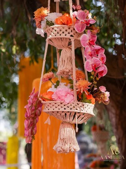 A beautiful two-tiered macrame hanging planter filled with pink orchids and other colorful flowers.