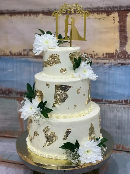 I love creating elegant, multi-tiered wedding cakes that taste as incredible as they look. This three-tier beauty features delicate buttercream, fresh white flowers, and hand-applied gold leaf for a touch of classic glamour.