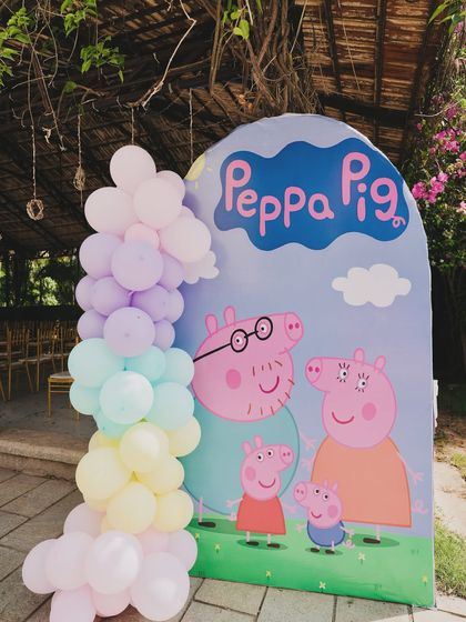 A Peppa Pig photo booth backdrop, featuring the whole family and a pastel rainbow balloon garland.