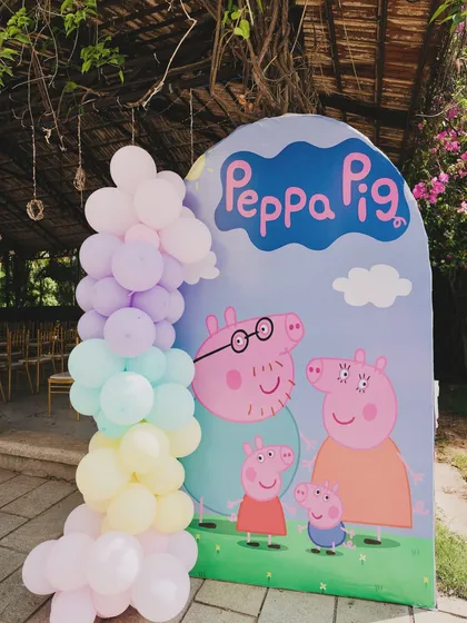 A Peppa Pig photo booth backdrop, featuring the whole family and a pastel rainbow balloon garland.
