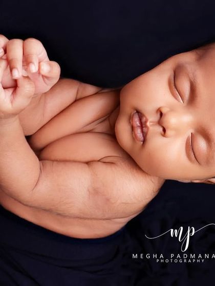 A simple and classic portrait of a newborn with their hands clasped, resting against a dark, contrasting background.