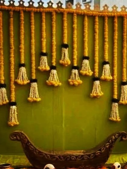 A beautiful and traditional backdrop design suitable for a Mehndi or Haldi function. The base is a simple green cloth, which makes the hanging garlands of marigolds and white jasmine flowers pop, creating a fresh and festive look.