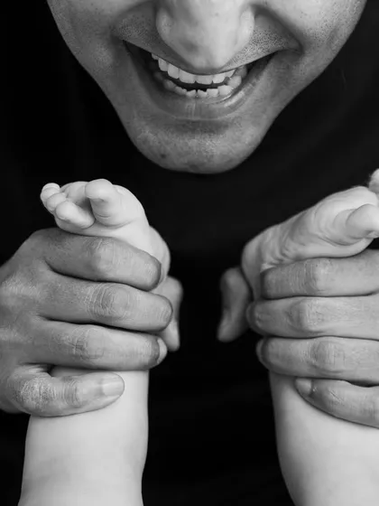 A father's joyful smile as he plays with his baby's feet. This unique, close-up black and white shot is full of love and personality.