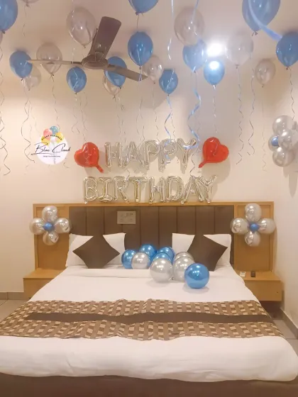 A romantic birthday bedroom decoration with silver 'Happy Birthday' foil letters and balloons on the ceiling and bed.