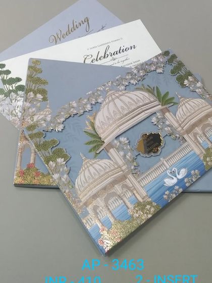 This pastel blue wedding card features a picturesque palace scene with swans on the water, highlighted with silver foil. The design includes two inserts for detailing your wedding and celebration events.