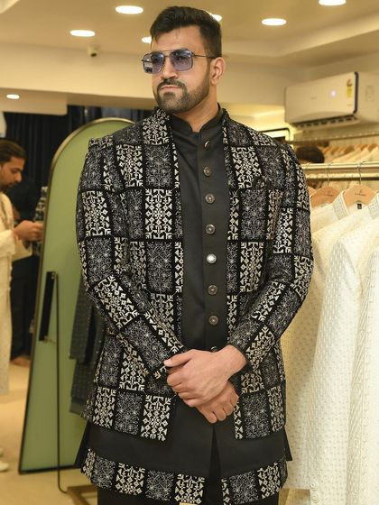 A client trying on a bold black and silver patterned jacket over a black kurta. This outfit is perfect for making a statement at a reception.