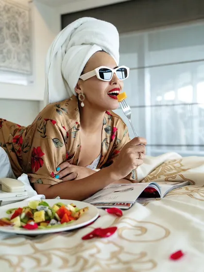 A model enjoying a fruit salad in bed during a hotel lifestyle shoot. The image conveys a sense of health, luxury, and leisurely mornings.