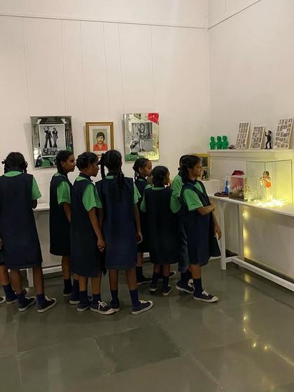 A group of students gathered around a display of miniature sculptures and objects related to Dr. Rajkumar.