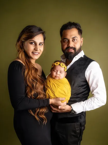 A lovely portrait of new parents presenting their precious baby to the world. The coordinated outfits and their happy expressions make this a heartwarming family photograph.