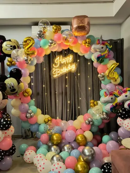 A fun-filled birthday setup combining Minnie Mouse and Unicorn themes. The decoration is built around a circular balloon arch in pastel colors, with a neon sign, character foil balloons, and a large Minnie Mouse figure made of balloons.