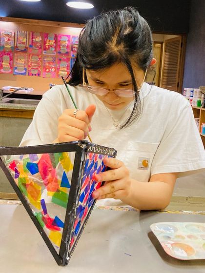 A close up of a student carefully painting the frame of her Diwali lantern, showing the fine motor skills and concentration involved.