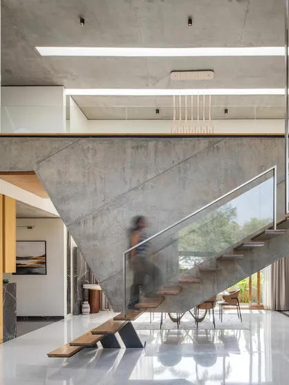 A person ascends the floating staircase, adding a sense of scale to the dramatic, suspended concrete wall. The transparency of the glass balustrade ensures the structure feels light and unobtrusive.