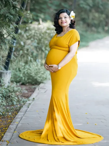 A solo portrait celebrating the beautiful curves of pregnancy. This mom-to-be looks radiant in a vibrant yellow gown, perfectly highlighting her baby bump against the soft greenery of the park path.