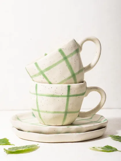 A clean, bright shot of stacked, hand-painted ceramic cups and saucers from Homesmith. The minimalist styling highlights the artisanal quality of the crockery.