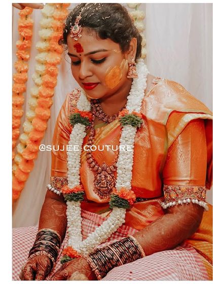 A candid shot of a bride during her Haldi ceremony. Her custom orange silk blouse is designed with subtle pearl embroidery on the sleeve cuffs, adding a touch of grace to her ceremonial look.
