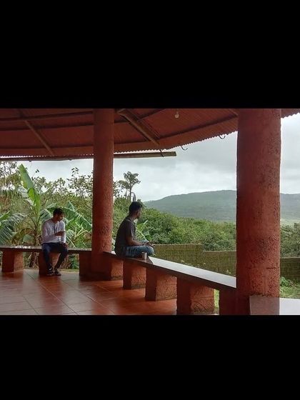 Two students in conversation on a veranda overlooking the lush greenery. The ashram provides many quiet spaces for personal reflection and connection with fellow aspirants.