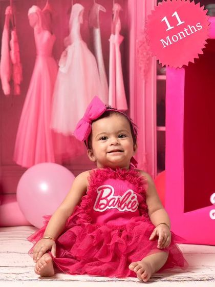 An 11-month-old baby girl enjoys her moment in the spotlight during a Barbie-themed milestone session. The set includes a custom Barbie box and accessories.