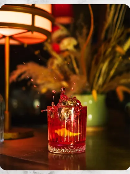 A classic Negroni captured in a moment of vibrant action. This image represents our dedication to perfecting timeless cocktails, focusing on quality ingredients and precise execution for a familiar yet elevated drinking experience.
