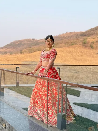 A full-length shot of the bride on a balcony overlooking a beautiful landscape. Her red lehenga stands out, and her makeup looks flawless even from a distance.