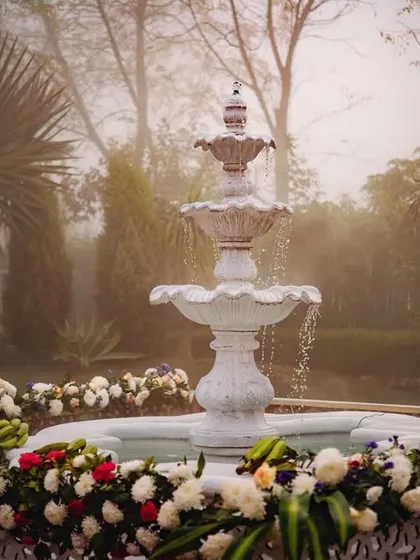 A serene white fountain surrounded by flowers, a beautiful and tranquil feature at the South Indian wedding venue.