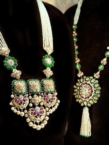 Two distinct polki masterpieces. One features a grand pendant with ruby accents, while the other is a long mala with a tassel, both showcasing the beauty of uncut diamonds and lush green beads for a festive look.