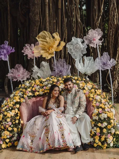 For this Mehendi, I designed a dreamy seating area with a plush pink sofa nestled in an arch of yellow and pastel flowers, creating a perfect, intimate spot for the couple.
