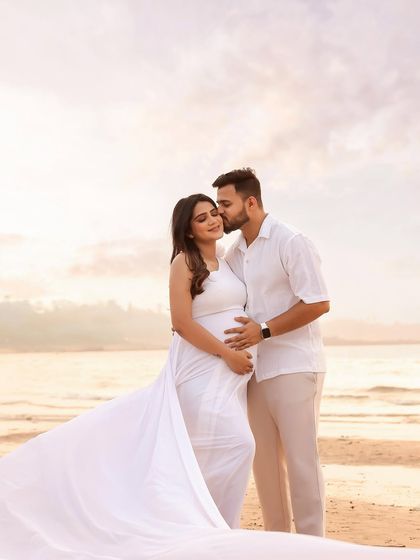 A gentle kiss on the cheek from her partner, as the white gown trails behind them on the sand. This image is the essence of a romantic and serene beach maternity session.