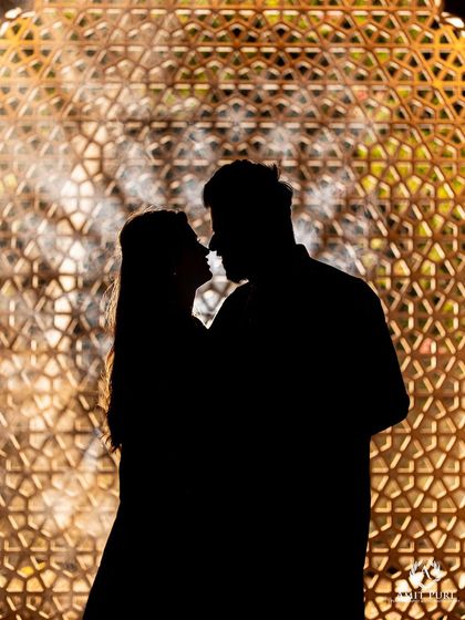 A beautiful silhouette shot against a backlit jaali screen. This artistic photo uses shadow and light to create a mysterious and romantic portrait, highlighting their closeness without showing details.