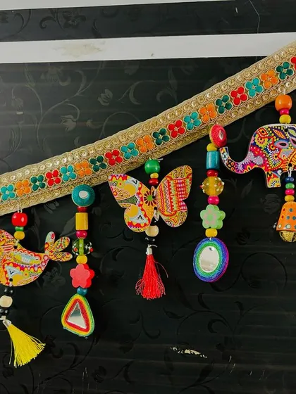 A close-up of the end of the 'Bageecha Toran', featuring a hand-painted elephant and a large brass bell.