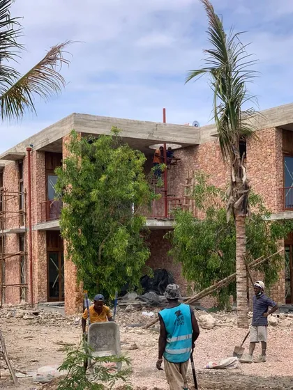 Workers on the phase two construction site at Kizikula. The building's coral stone facade is visible, a locally sourced material that gives the project a strong sense of place.