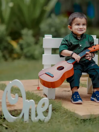 A little musician in the making. This happy moment is from a first birthday photoshoot, where we used a tiny guitar and the "One" sign to capture his cheerful personality. These themed shoots are all about fun.