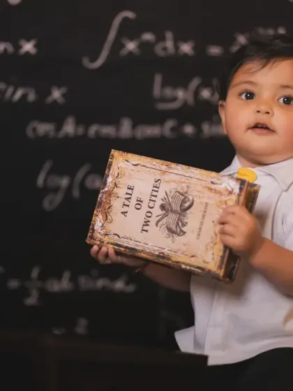 A close-up shot of a baby holding a classic book against the chalkboard backdrop.