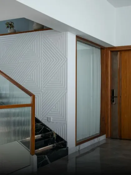 Details of a staircase with a textured geometric wall panel. The design creates a dynamic interplay between the clean lines of the glass railing and the intricate pattern on the wall.