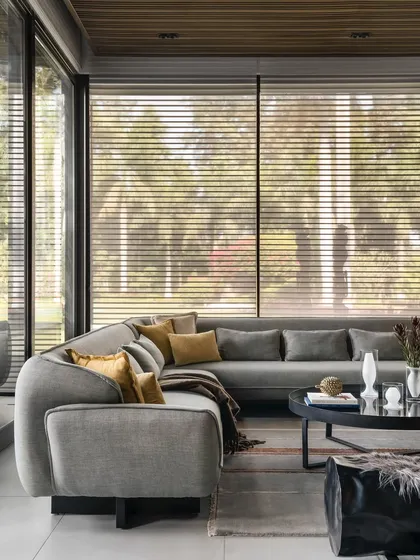Inside the pool house, comfort is key. I selected this large, curved sectional sofa to create an intimate lounge area that still feels open to the surrounding views. The neutral grey fabric is complemented by warm mustard pillows, adding a pop of color that echoes the natural light.