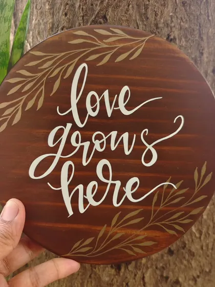 The "love grows here" plaque placed against a tree trunk, emphasizing the natural, earthy feel of our wooden decor.