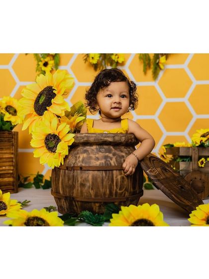 A sweet portrait of a baby girl in a wooden barrel, surrounded by sunflowers. Her calm and curious expression is beautifully captured in this shot.