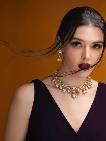 This shot captures a sense of movement and drama. The focus is on the model's expression and the elegant gold necklace, creating a dynamic and engaging portrait for the jewelry brand.