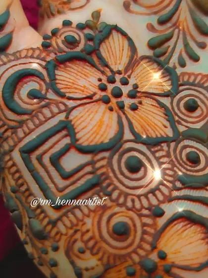 A sparkling close-up of the floral details. The light catches the fresh henna paste, making it look like it's glowing.